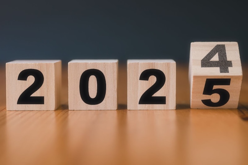 Four wooden cubes with black numbers displaying the year 2024. Last cube is tipping to show number 5